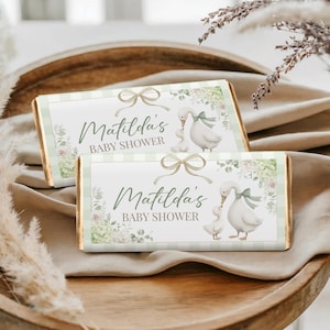 May include: Two chocolate bar wrappers with a baby shower theme. The wrappers feature a green and white striped background, a bow, and an illustration of a mother goose and gosling. The text "Matilda's BABY SHOWER" is printed on the wrappers.