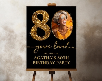 May include: Black and gold birthday party sign with a photo of a woman and the text "80 years loved" and "Welcome to Agatha's 80th Birthday Party".