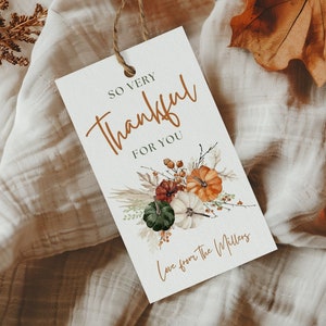 Może przedstawiać: Prostokątna etykieta prezentowa z napisem "So Very Thankful For You" w brązowym skrypcie. Etykieta zawiera akwarelową ilustrację dyni, liści i liści. U góry przymocowany jest sznurek.