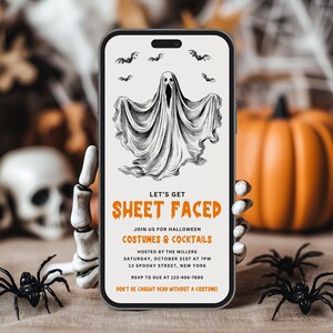 Może przedstawiać: Smartfon wyświetla zaproszenie na imprezę Halloween. Zaproszenie zawiera ilustrację ducha z tekstem "LET'S GET SHEET FACED" oraz szczegóły dotyczące imprezy kostiumowej. Czarne pająki i szkieletowa dłoń na pierwszym planie.