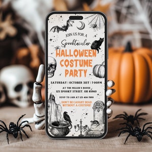 May include: A smartphone displays a Halloween Costume Party invitation. The invitation features a bat, spiderwebs, a black cat, a skull, and a pumpkin. The text reads "Spooktacular Halloween Costume Party" with date, time, and location details. Black plastic spiders and a skeleton hand are in the foreground.
