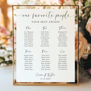 May include: A gold-framed seating chart with the words "our favorite people" and "your seat awaits" in elegant script. The chart lists names under the numbers one through six, with the names Sienna & Taylor and the date 07.12.20XX at the bottom.