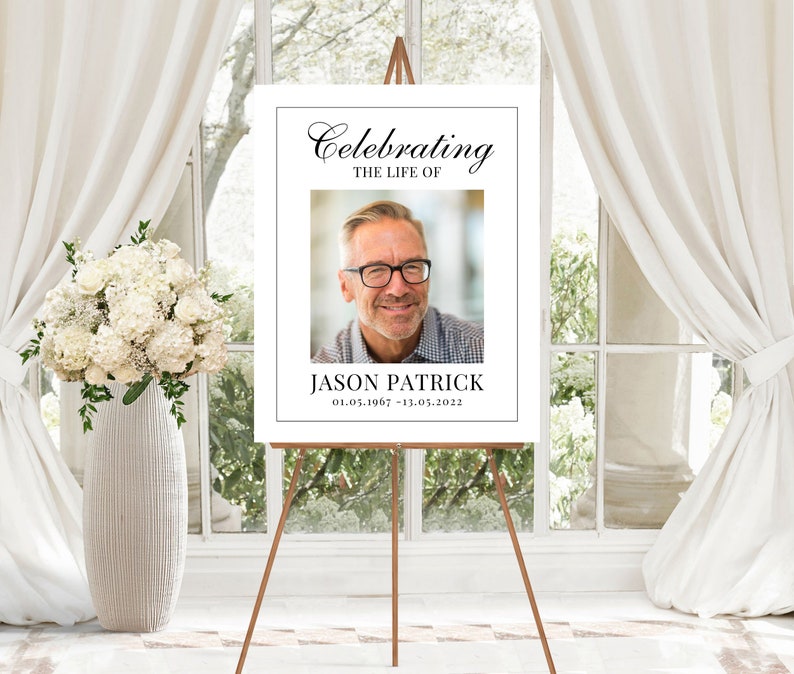 May include: A white memorial sign with black text that reads "Celebrating the Life of Jason Patrick 01.05.1967 - 13.03.2022". A photo of a man with glasses is in the center of the sign.