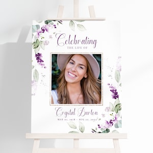 May include: A white memorial sign with a gold frame and purple floral accents. The sign reads "Celebrating the Life of Crystal Burton May 01, 1978 - Aug 22, 2022". A photo of a woman is in the center of the sign.