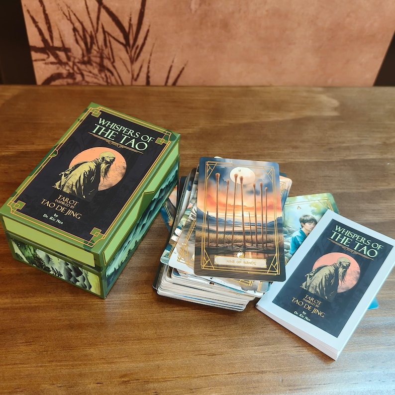 Op de afbeelding: Een tarotkaartspel getiteld "Whispers of the Tao" met een groene en zwarte doos. De doos en kaarten bevatten illustraties van een figuur in een cirkel en andere afbeeldingen. Het spel bevat de tekst "Tarot Tao De Jing".