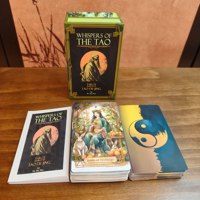 Op de afbeelding: Een tarotkaartspel genaamd "Whispers of the Tao" met een doos met een gebaarde figuur. Het spel bevat ge&iuml;llustreerde kaarten, waaronder een met het opschrift "Queen of Pentacles" en een andere met een yin-yang symbool.
