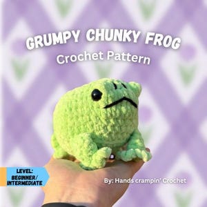May include: A light green, chunky crochet frog with black eyes and a grumpy expression. The text "GRUMPY CHUNKY FROG Crochet Pattern" is displayed above the frog. The text "LEVEL: BEGINNER/INTERMEDIATE" is on the left. The text "By: Hands crampin' Crochet" is on the right.