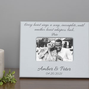 May include: White picture frame with a black and white photo of a couple laughing. The frame has a quote from Plato: "Every heart sings a song, incomplete, until another heart whispers back." The frame is personalized with the names "Amber & Peter" and the date "04.20.2021".