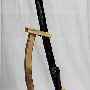 Pu&ograve; includere: Una katana nera con una tsuba (guardia) dorata e una saya (fodero) bianca e nera &egrave; esposta su un supporto in legno.