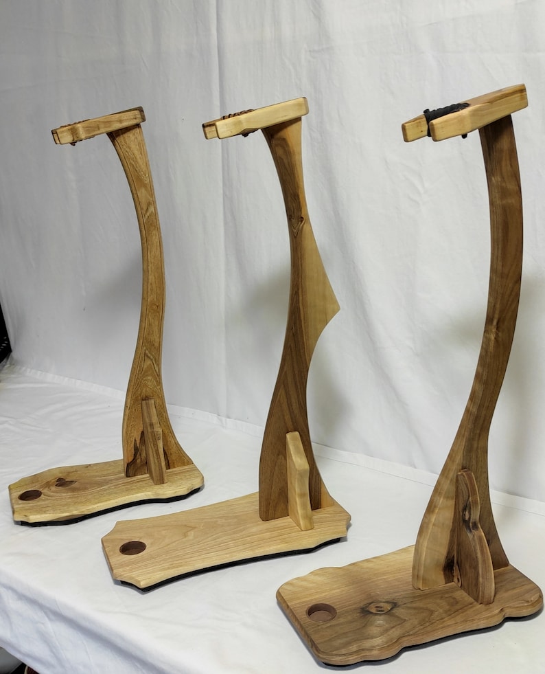 Pu&ograve; includere: Tre supporti per chitarra in legno con un design curvo. I supporti sono in legno marrone chiaro e hanno una finitura naturale.
