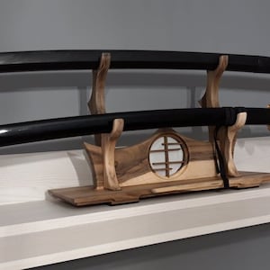 Puede incluir: Dos katanas negras con detalles dorados se muestran en un soporte de madera con un diseño de ventana decorativo.