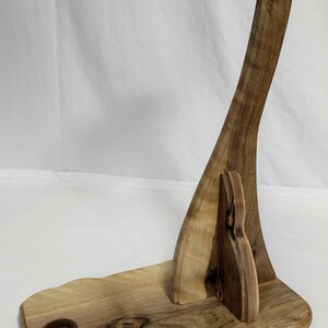 Pu&ograve; includere: Un supporto per chitarra in legno con un manico curvo e una base con un piccolo foro. Il supporto &egrave; in legno marrone chiaro con venature marrone scuro.