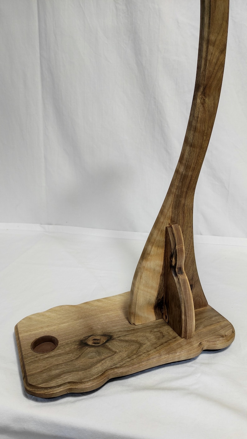 Pu&ograve; includere: Un supporto per chitarra in legno con un manico curvo e una base con un piccolo foro. Il supporto &egrave; in legno marrone chiaro con venature marrone scuro.