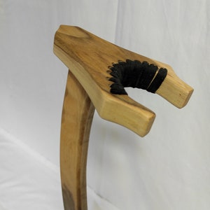 Pu&ograve; includere: Un cavalletto per chitarra in legno con un cordoncino nero avvolto attorno al supporto del manico.