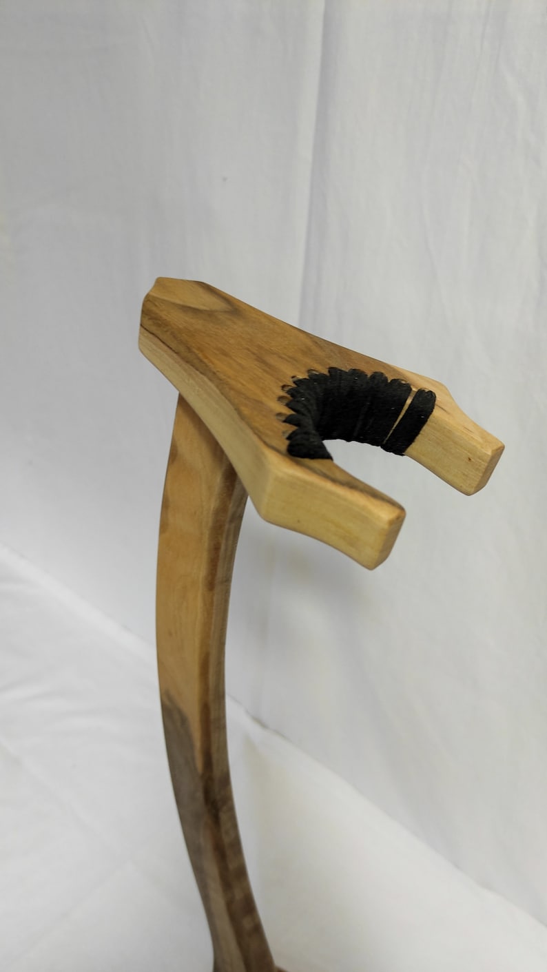 Pu&ograve; includere: Un cavalletto per chitarra in legno con un cordoncino nero avvolto attorno al supporto del manico.