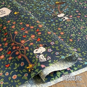 Può includere: Tessuto blu scuro con un design floreale e ad albero, con i personaggi di Snoopy e Woodstock. Il tessuto ha un aspetto vintage, con il testo "Vintage PEANUTS" e fumetti con "HEE HEE HEE".