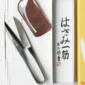 May include: A pair of silver and black sewing scissors with a brown leather sheath. The scissors are open, revealing the sharp blades. Japanese text is visible on the packaging.