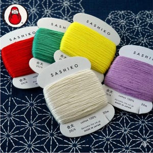 Può includere: Cinque rocchetti di filo da ricamo Sashiko nei colori rosso, verde, giallo, bianco e viola. Ogni rocchetto contiene 30 metri di filo 100% cotone, con le scritte Sashiko, 20/6, cotton 100%, daruma-ito.co.jp e MADE IN JAPAN.