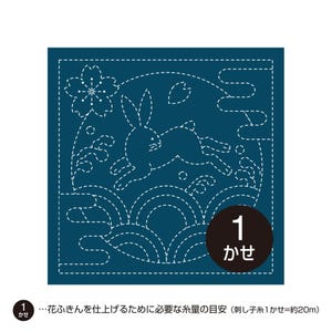 以下が含まれることがあります： 濃い青色の正方形の布地に、白の点線で刺繍されたウサギ、波、桜、雲の模様が描かれています。右下の濃い茶色の円の中には白い文字で「1 かせ」と記されており、下部には「1 かせ…花ふきんを仕上げるために必要な糸量の目安（刺し子糸1かせ=約20m）」という説明文があります。