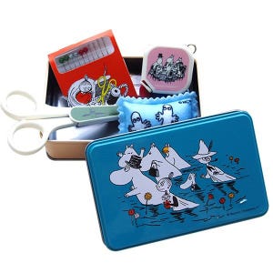 May include: A blue rectangular tin sewing kit with Moomin characters. Inside the tin are a red needle case, a pink tape measure, a blue pin cushion, and scissors. The tin is open, displaying the sewing supplies.