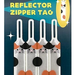 Op de afbeelding: Vier transparante reflecterende ritssluitingen met kattenontwerpen. Elke tag heeft een kattengezicht met oranje en zwarte accenten, een zwarte cirkel en een oranje vlinderdas. De tekst "REFLECTOR ZIPPER TAG" is inbegrepen.
