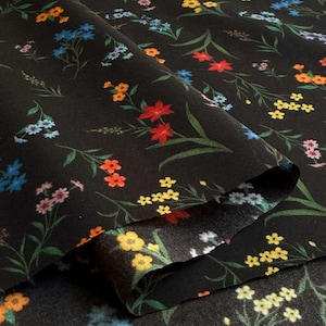 May include: Black fabric with a colorful floral pattern. The design features red, yellow, blue, orange, and pink flowers with green stems and leaves. The fabric is folded, showing the underside.
