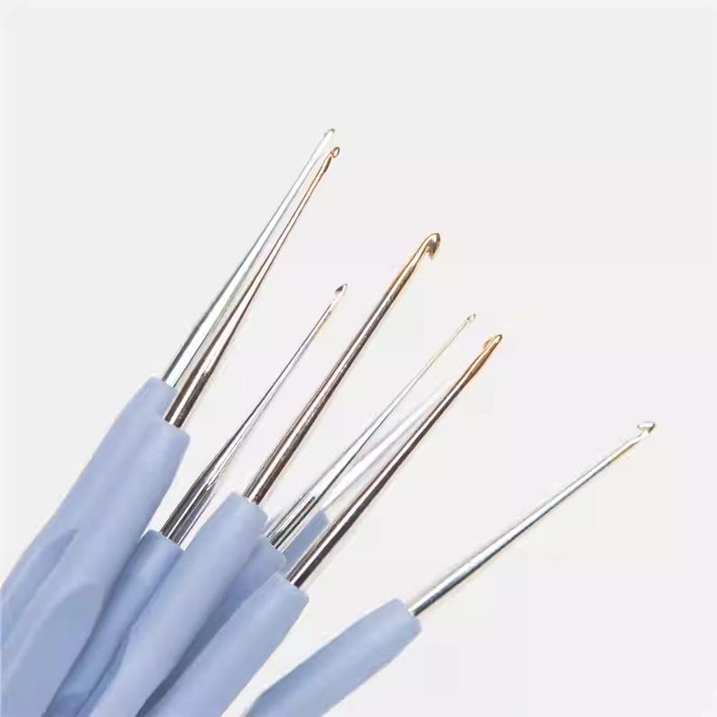 A group of crochet hooks in various sizes and colors, including silver, gold, and blue, arranged against a white background.