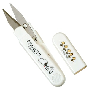 May include: White and silver Peanuts-themed scissors with a protective cover. The scissors feature a Snoopy illustration and the word "PEANUTS". The cover displays a pattern of Woodstock characters. © 2022 PNTS is printed on the scissors and cover.