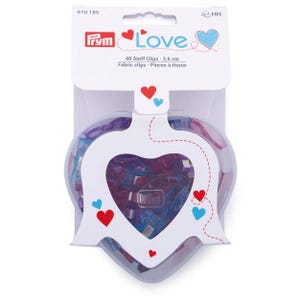 May include: Prym fabric clips in a heart-shaped container. The package contains 40 clips, each 2.6 cm long. The packaging features the word "Love" and decorative hearts in red and blue.