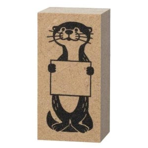 May include: A rectangular wooden stamp featuring a black illustration of an otter holding a blank sign. The otter has a smiling face and is standing upright. The stamp is made of light brown wood.