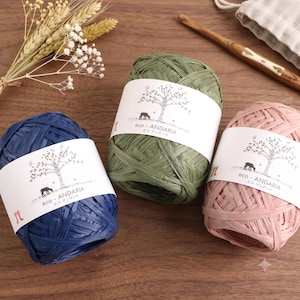 May include: Three balls of Eco-Andaria raffia yarn in navy blue, olive green, and dusty pink. Each ball features a white paper label with a black illustration of a tree and a deer, along with the text eco-ANDARIA and Japanese characters.