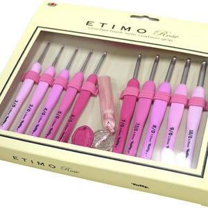 Op de afbeelding: Een set Etimo Rose haaknaalden met kussengrepen, in een cr&egrave;mekleurige doos. De haaknaalden zijn in verschillende roze tinten, met maten van 2/0 tot 10/0. De doos bevat een roze kwast en een klein roze accessoire.