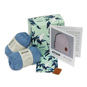 May include: A craft kit with blue yarn balls, a light green box with a Moomin design, and a beanie pattern. The kit includes a leather tag and printed instructions. The box and yarn labels display the text "MOOMIN x NOVITA".