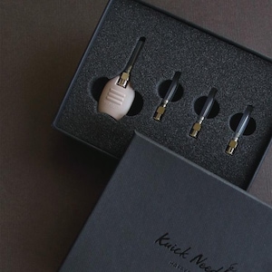 Könnte beinhalten: Eine schwarze Box mit dem Text "Knick Needle Happy Bears" auf der Vorderseite. Die Box enthält ein kleines, hellbraunes Gerät mit einer goldenen Oberseite und vier schwarzen Nadeln.