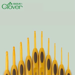 Puede incluir: Un conjunto de ganchillos de diferentes tamaños, con mangos amarillos y ganchos dorados. Los mangos tienen un agarre ovalado marrón oscuro. La marca "Clover" es visible en la esquina superior izquierda.