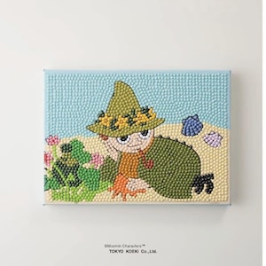 May include: A rectangular bead art piece featuring a character wearing a green hat with yellow flowers, a green cloak, and an orange shirt. The scene includes a sandy beach, blue sky, green foliage with pink flowers, and two seashells. Text reads Moomin Characters TOKYO KOEKI Co., Ltd.