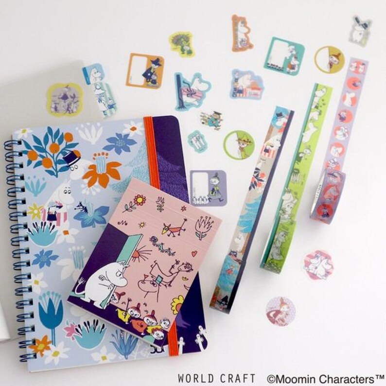 various colorful items, including a notebook, stickers, and a pen, arranged on a white surface.