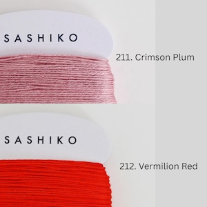 two spools of thread, each with a different color: one is a pinkish-red color and the other is a deep red color. The text above the spools reads "SASHIKO" and "211. Crimson Plum" respectively, indicating the brand and color of the thread.