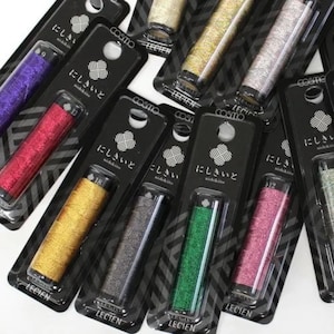 May include: A selection of metallic thread spools in colours such as purple, red, gold, silver, green, and pink. Each spool is packaged in a black and clear plastic container with Japanese text.