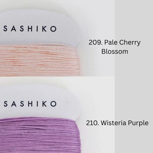 two spools of thread, each with a different color: one is pale pink and the other is purple. The text above the spools reads "SASHIKO" and below them, "209. Pale Cherry Blossom" and "210. Wisteria Purple".