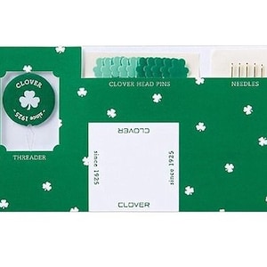 May include: A green Clover sewing kit with white shamrock accents. The kit includes a threader, Clover head pins, and needles. The Clover logo is visible, along with the text "since 1925".