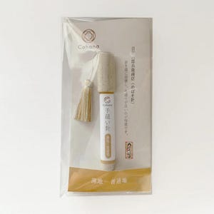 A package containing a small, cylindrical object with a tassel attached, which appears to be a product from the brand "Cohana".