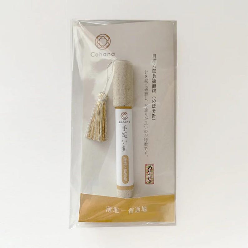 A package containing a small, cylindrical object with a tassel attached, which appears to be a product from the brand "Cohana".