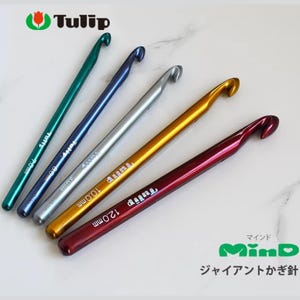 Op de afbeelding: Een set van vijf kleurrijke Tulip haaknaalden in verschillende metallic tinten: groen, blauw, zilver, goud en rood. Elke haaknaald heeft een gebogen uiteinde en een maatmarkering in millimeters. De afbeelding bevat het Tulip-logo en Japanse tekst.