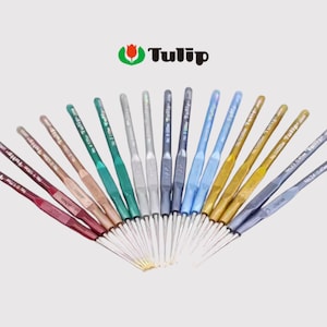 May include: A collection of Tulip crochet hooks in various colors, including red, green, silver, blue, and gold. The hooks are arranged in a fan shape, with the brand name "Tulip" and a logo visible at the top.