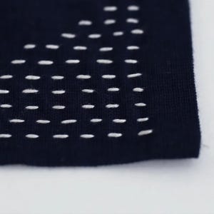 A close-up view of a dark fabric with white stitching, creating a patterned design.