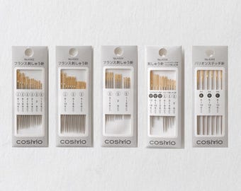 May include: Five packs of embroidery needles, each containing a different selection of needle sizes. The packaging features Japanese text and the brand name "cosmo". The needles are gold-coloured and presented in clear plastic sleeves.
