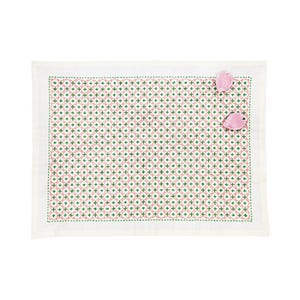 May include: A rectangular white placemat featuring a repeating geometric pattern of small green crosses and interlocking pink circles. The border is stitched in green thread, and two small, light pink, petal-shaped ornaments are attached.