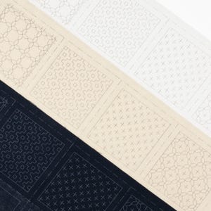以下が含まれることがあります： クリーム、白、ネイビーブルーの生地見本を斜めから見た画像。各見本には、ライトグレーの異なる幾何学模様が施されています。模様には、クロスハッチング、円、幾何学的な形が含まれています。測定値は適用されません。