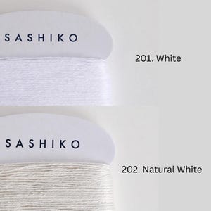 two spools of yarn, each with a different color: one labeled "SASHIKO" in black text on a white background, and the other labeled "201. Natural White" in black text on a white background.